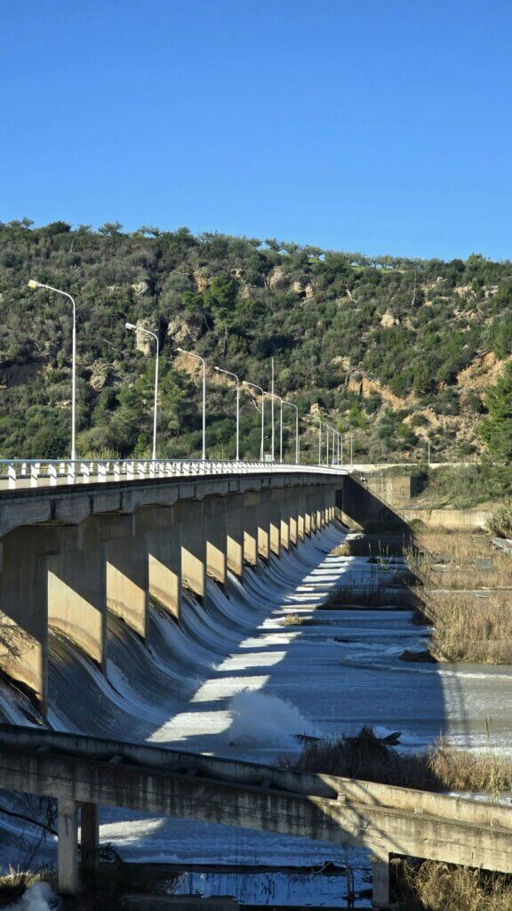 A scenic view of an architectural bridge spanning over a flowing river with lush hills in the background.